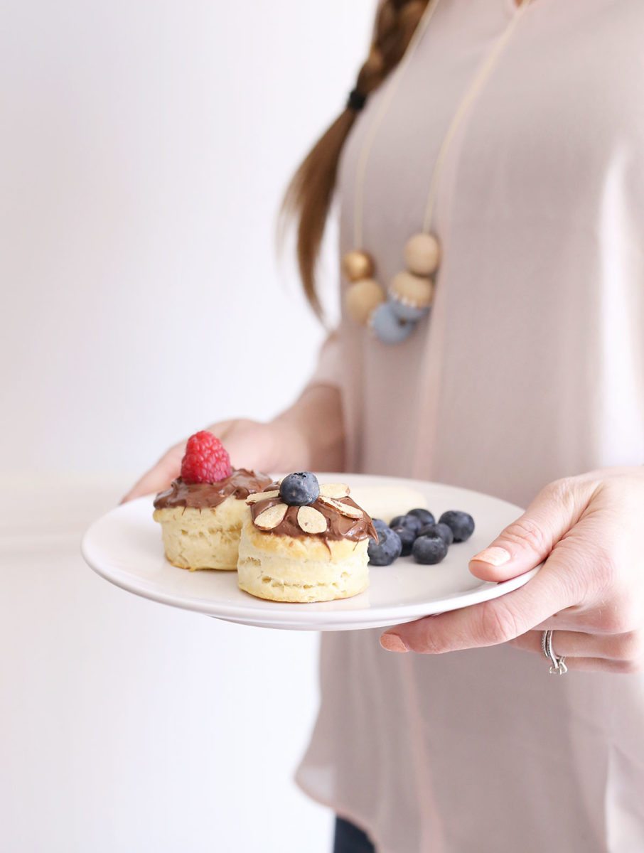 Hands holding plate with two biscuits with Nutella and fruit