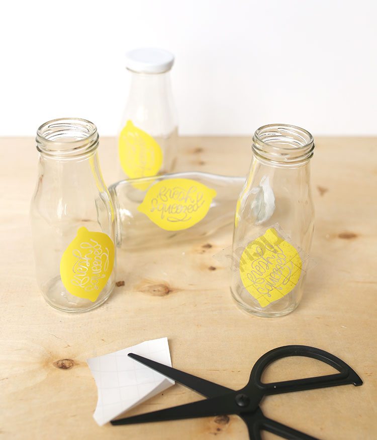 Bottle lids and glass milk bottles with handmade DIY vinyl lemon decals on a wooden background