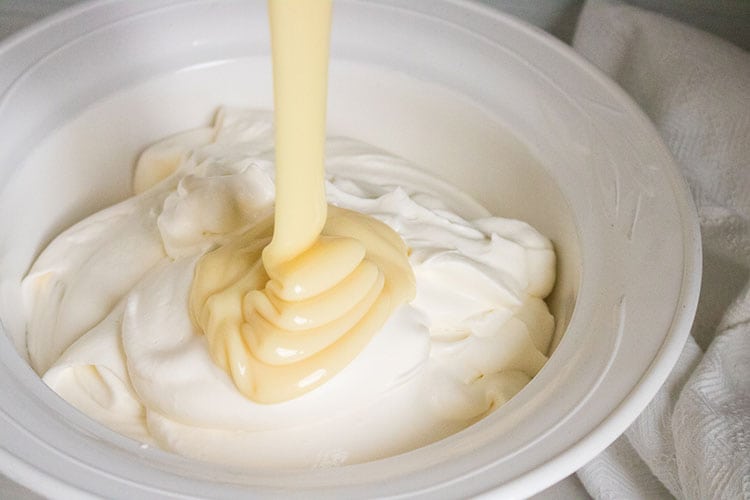 Black Cherry No Churn Ice Cream Recipe Step 3 - Sweetened condensed milk dripping into a white bowl of ice cream mixture.