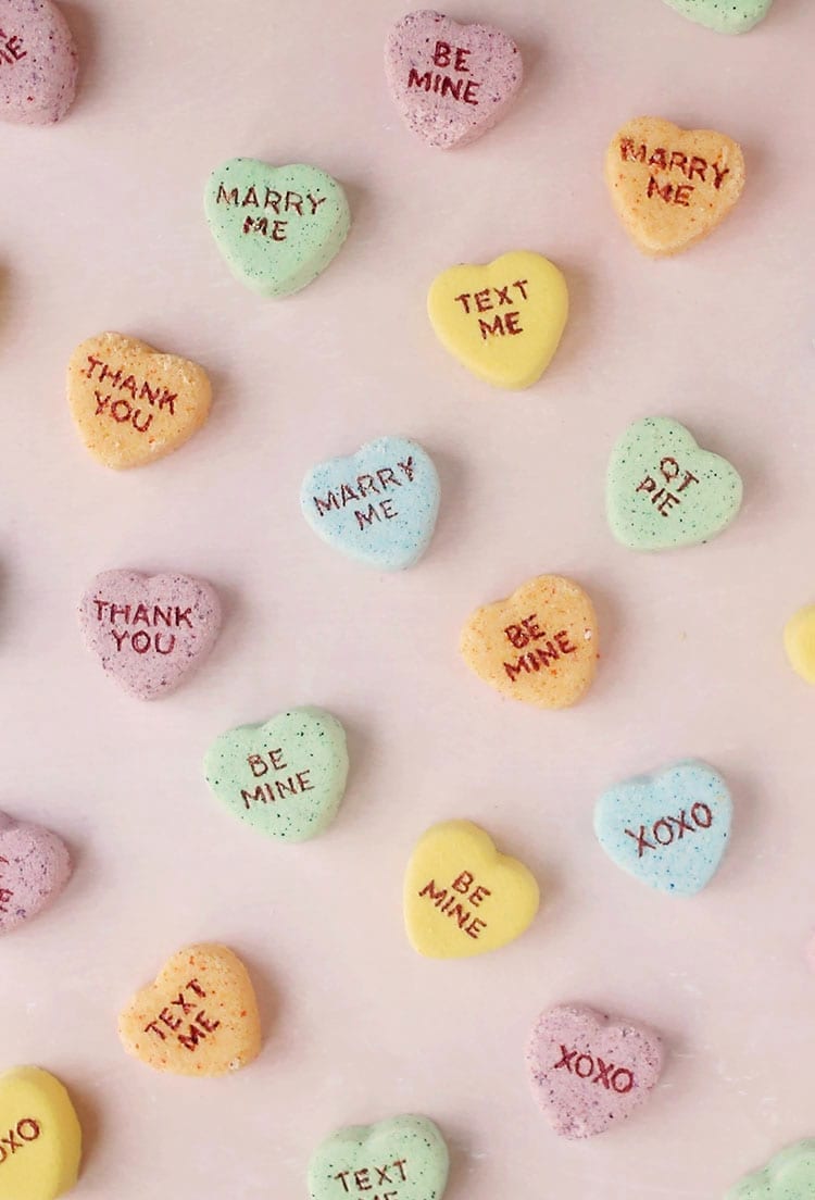 Yellow, orange, blue, and green conversation heart Valentine's Day bath bombs on a pink background