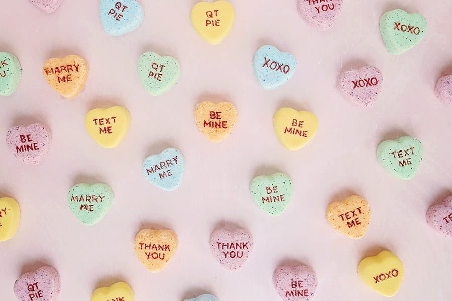 Yellow, orange, blue, and green conversation heart Valentine's Day bath bombs on a pink background