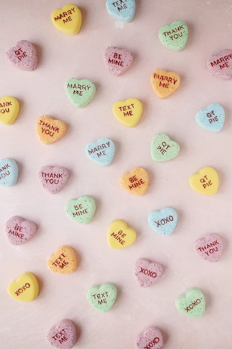 Yellow, orange, blue, and green conversation heart Valentine's Day bath bombs on a pink background