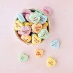 Yellow, orange, blue, and green conversation heart Valentine's Day bath bombs in a bowl on a pink background