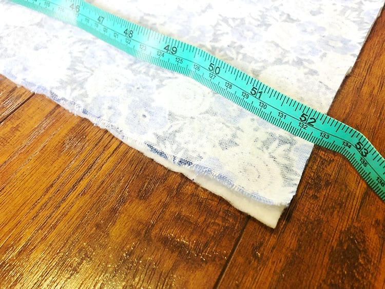Teal measuring tape laid across two sheets of fabric on a wooden floor