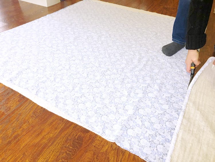 Person's hand cutting sheet of fabric on a wood floor