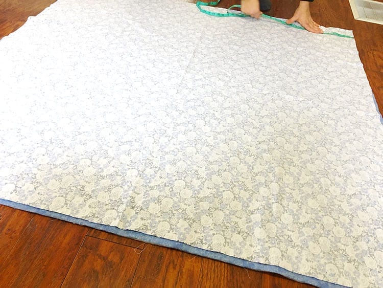 Hands measuring a large square of fabric on a wood floor