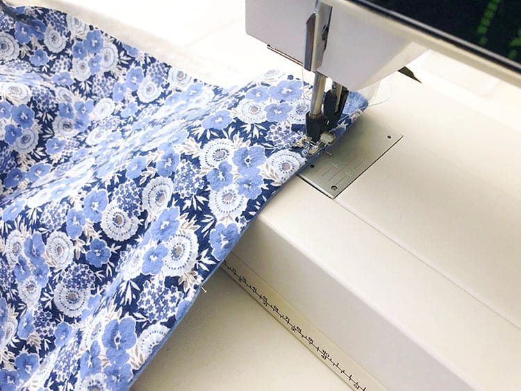 Sewing machine sewing a straight stitch on blue floral fabric