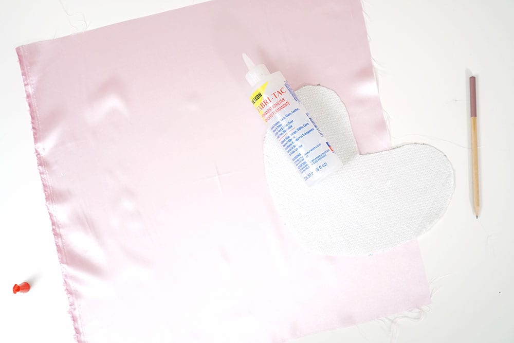 Bottle of Beacon Adhesives Fabri-Tac glue on top of a mermaid sequin fabric heart and pink satin to make a magic sequin pillow