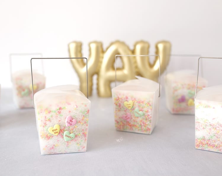 Clear takeout containers filled with conversation hearts Valentine's Day bath salts recipe on a grey background in front of a YAY sign in gold letters