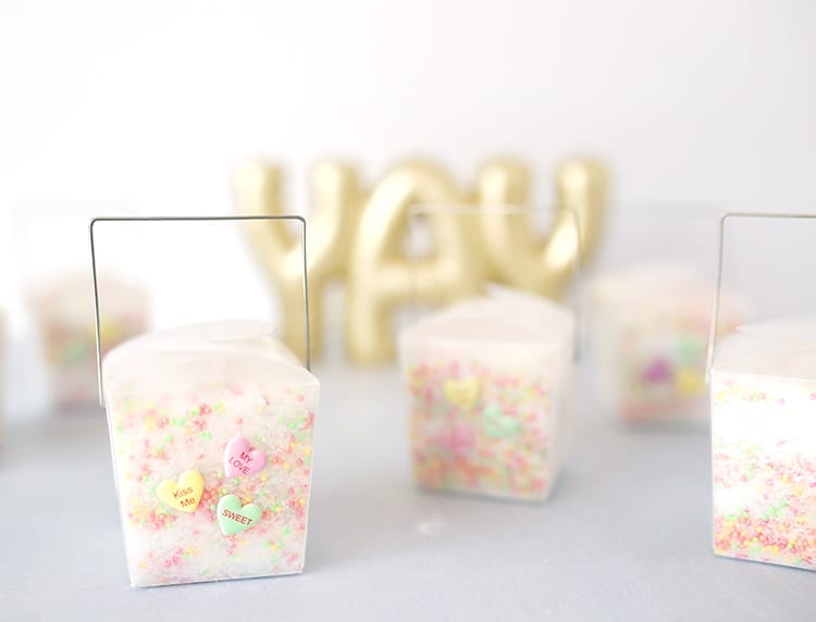 Clear takeout containers filled with conversation hearts Valentine's Day bath salts recipe on a grey background in front of a YAY sign in gold letters