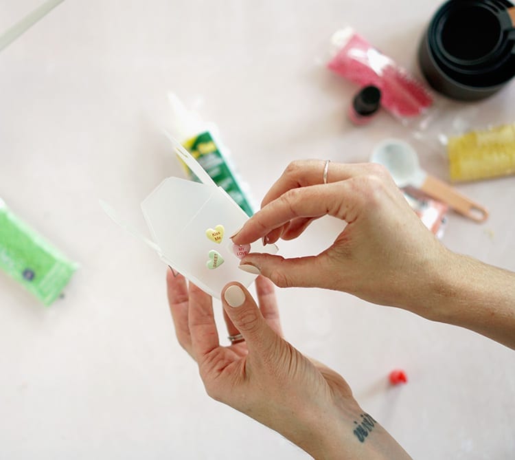 Caucasian hand applying conversation hearts stickers to a clear takeout box