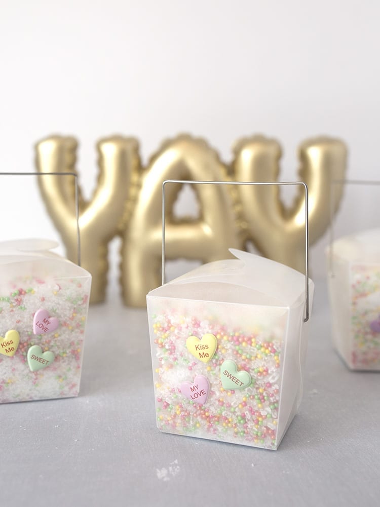 Clear takeout containers filled with conversation hearts Valentine's Day bath salts recipe on a grey background in front of a YAY sign in gold letters