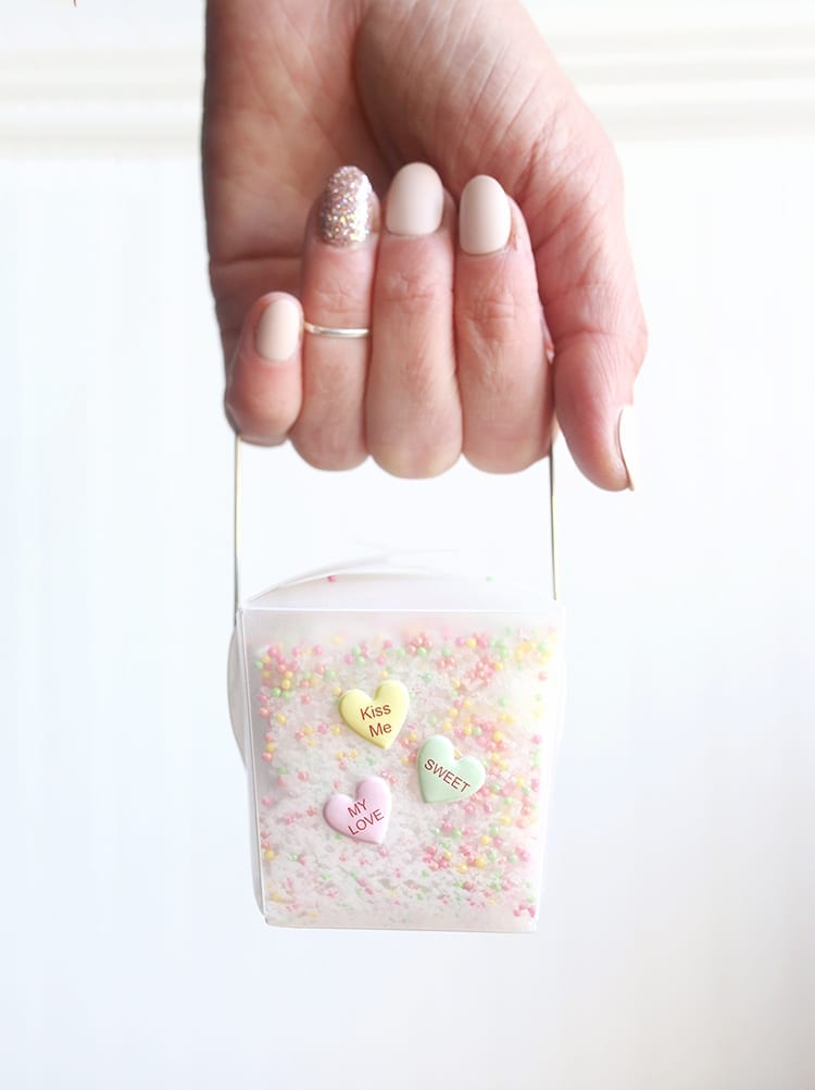 Caucasian hand holding a clear takeout container of conversation hearts Valentine's Day bath salts