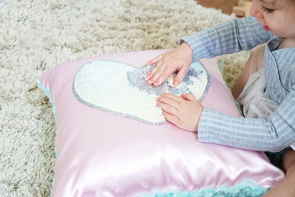 Toddler hands playing with a pink heart shaped magic sequin pillow