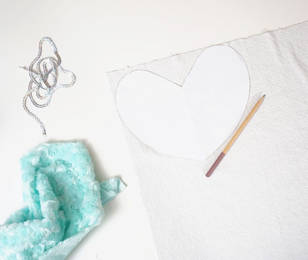 Paper heart and pencil on top of flip sequin fabric next to turquoise faux fur and a strip of sequin trim for a flip sequin pillow
