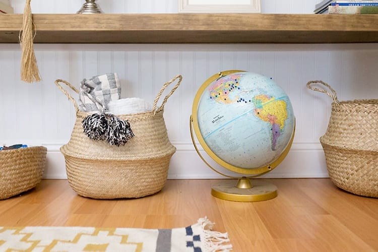Baskets and globe on wooden floor in front of yellow and white geometric-patterned rug