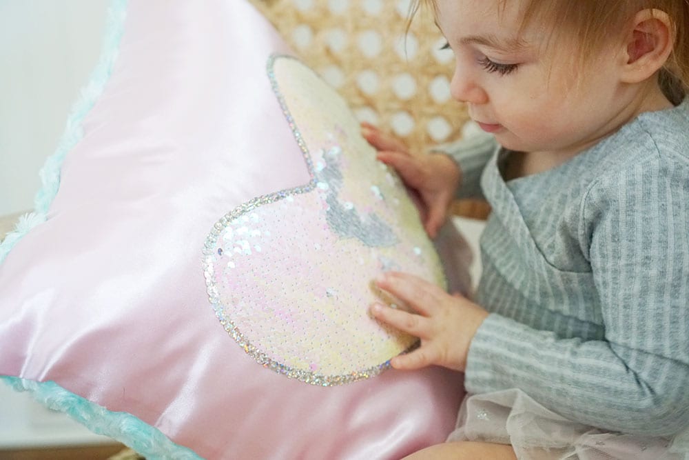 Toddler hands playing with a pink heart shaped flip sequin pillow