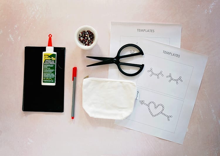 Beacon Adhesives Gem-Tac glue, graphite transfer paper, black scissors, a small white canvas pouch, a dish of red rhinestone, and white printouts on a pink background