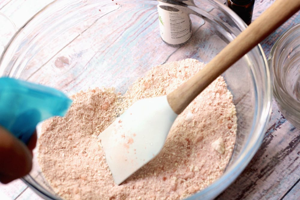 Spatula mixing pink Himalayan salt bath bomb recipe in a glass bowl