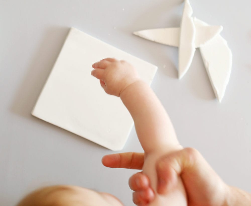 Father holding baby's arm over air dry clay on a silicone baking mat to make a diy baby clay handprint keepsake frame