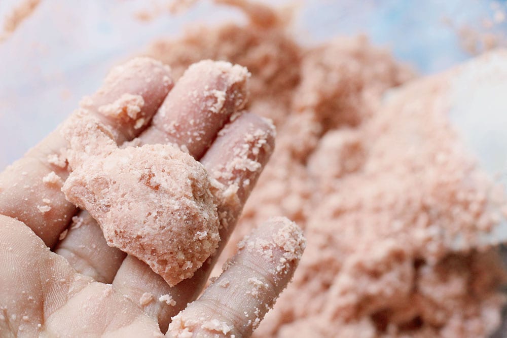 Caucasian hand holding clump of pink Himalayan salt bath bomb mixture