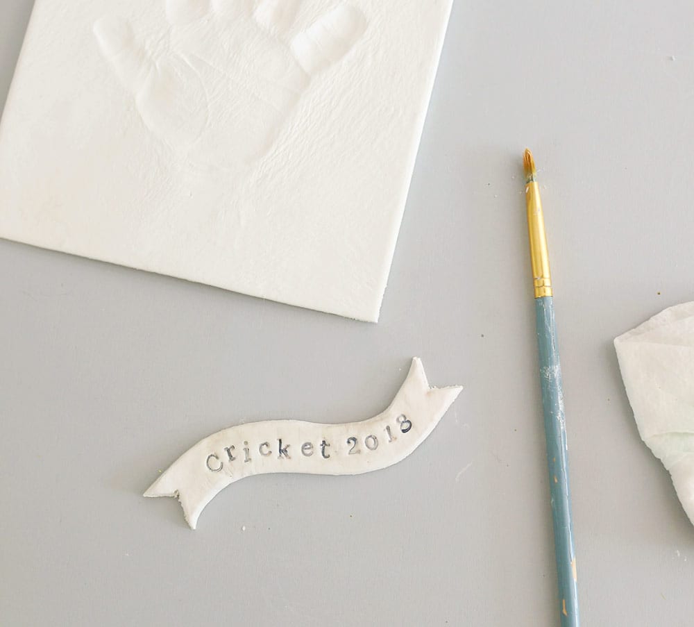 Letters stamped on banner on air dry clay on a silicone baking mat to make a diy baby clay handprint keepsake frame