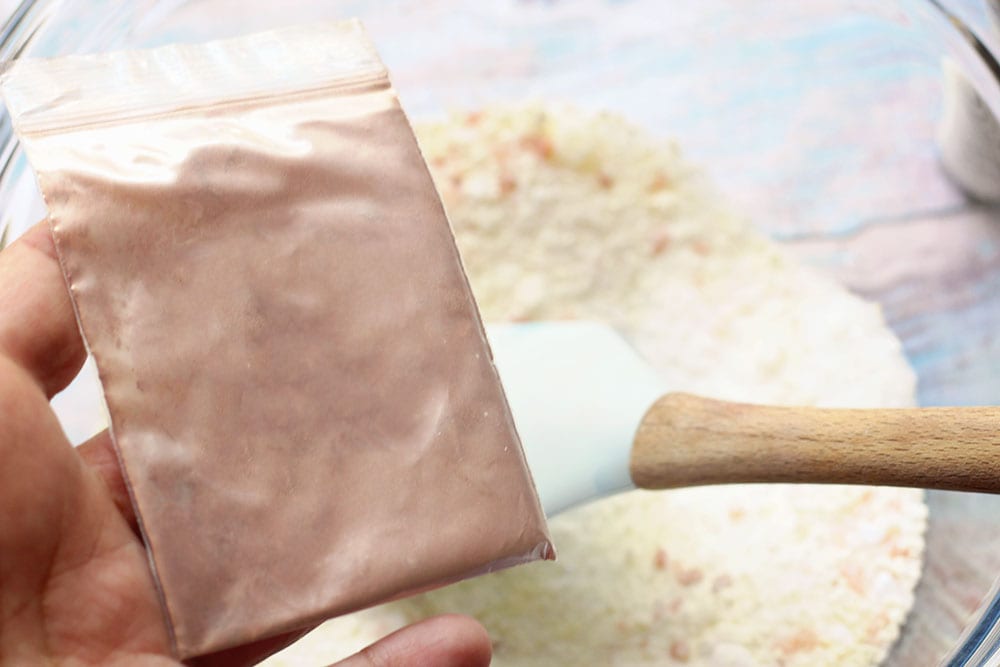 Caucasian hand holding small baggie of rose gold mica powder for recipe for pink Himalayan salt bath bombs