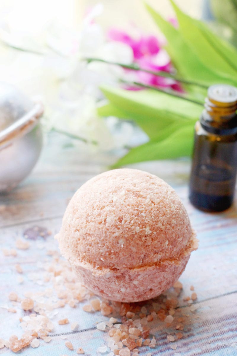 Recipe for pink Himalayan salt bath bomb on a wooden background with an essential oil bottle