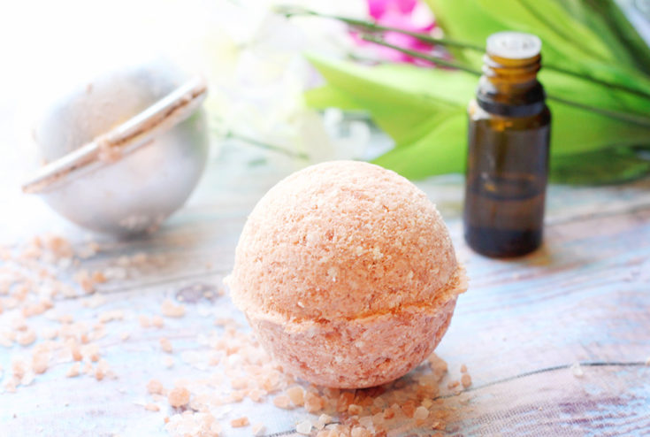 Pink Himalayan salt bath bomb on a wooden background with an essential oil bottle