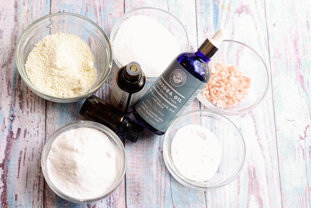 Ingredients for recipe for pink Himalayan salt bath bombs in glass bowls on a wood background