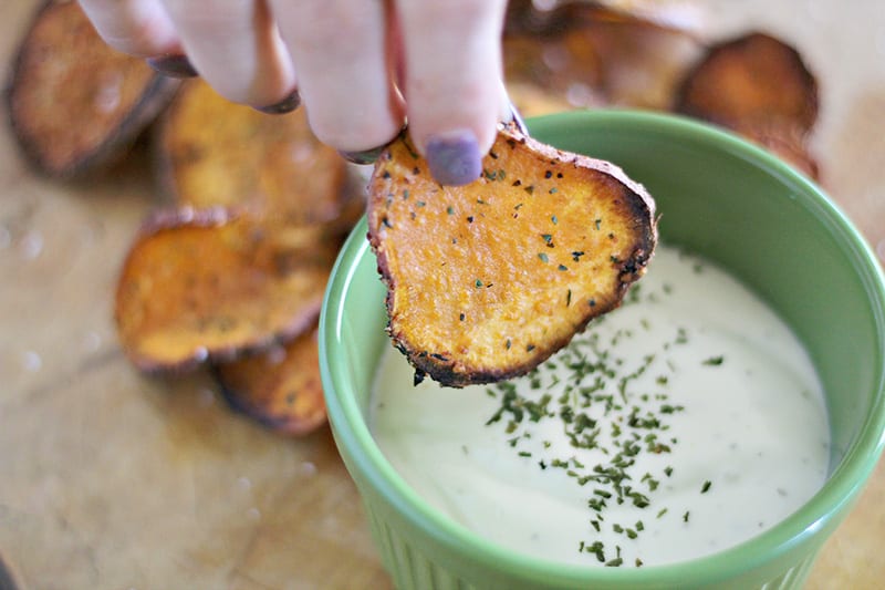 Woman's hand dipping a crispy baked sweet potato chips recipe into ranch dressing