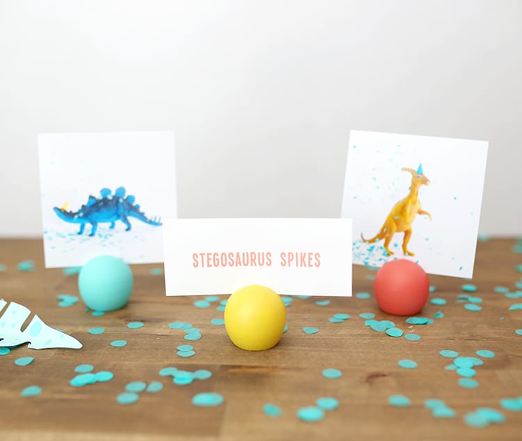 Three colorful wooden DIY place card holders with pictures from a dinosaur party