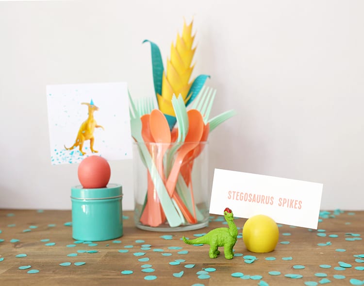 DIY place card holder at a dinosaur birthday party setup with yellow, coral, and teal accessories