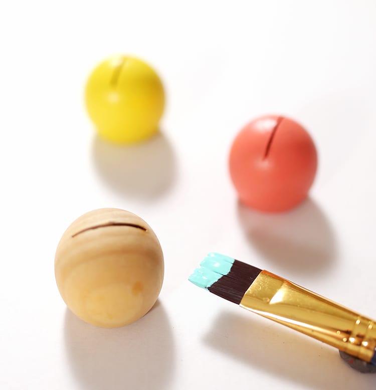 Three wooden balls being painted for DIY place card holders