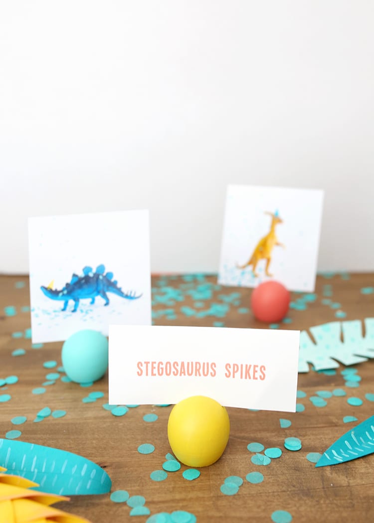 Three colorful wooden DIY place card holders with pictures from a dinosaur party