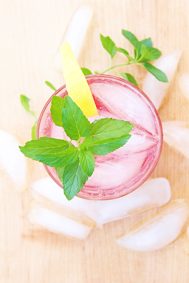 Cocktail in a rocks glass with cherry lemonade drink and a sprig of mint next to a pool for summer